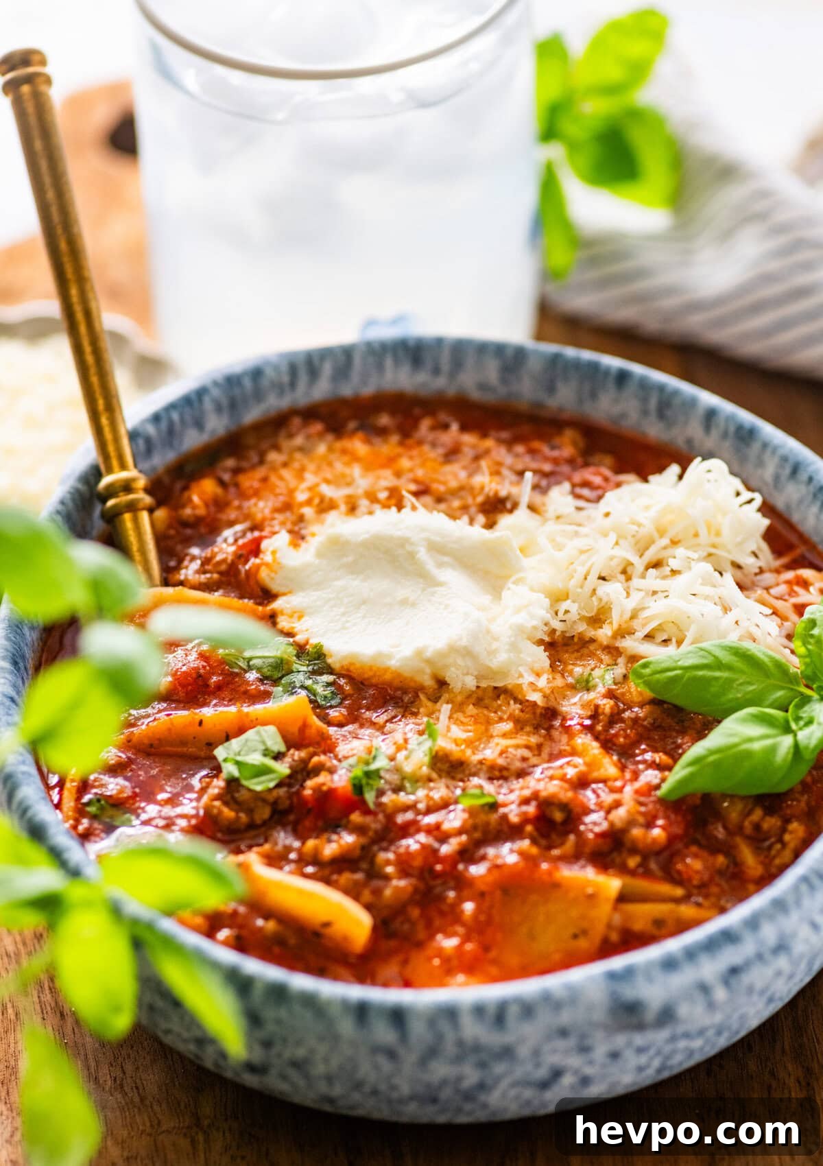 lasagna soup in a bowl topped with basil and cheese with more toppings in the background.