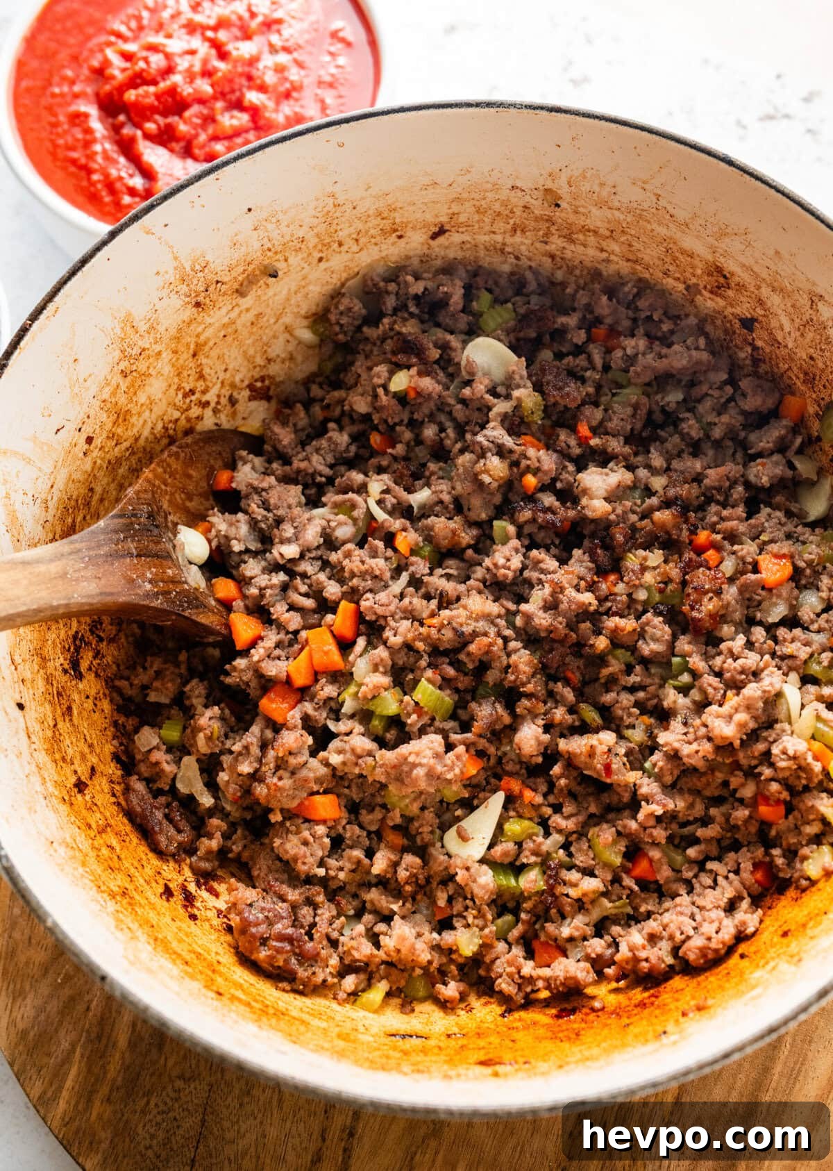 spoon showing browned meat previously added to the same pot as the vegetables.
