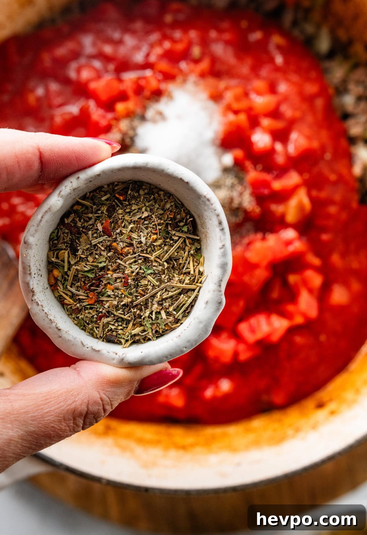 holding Italian seasoning in a bowl over the pot of lasagna soup.