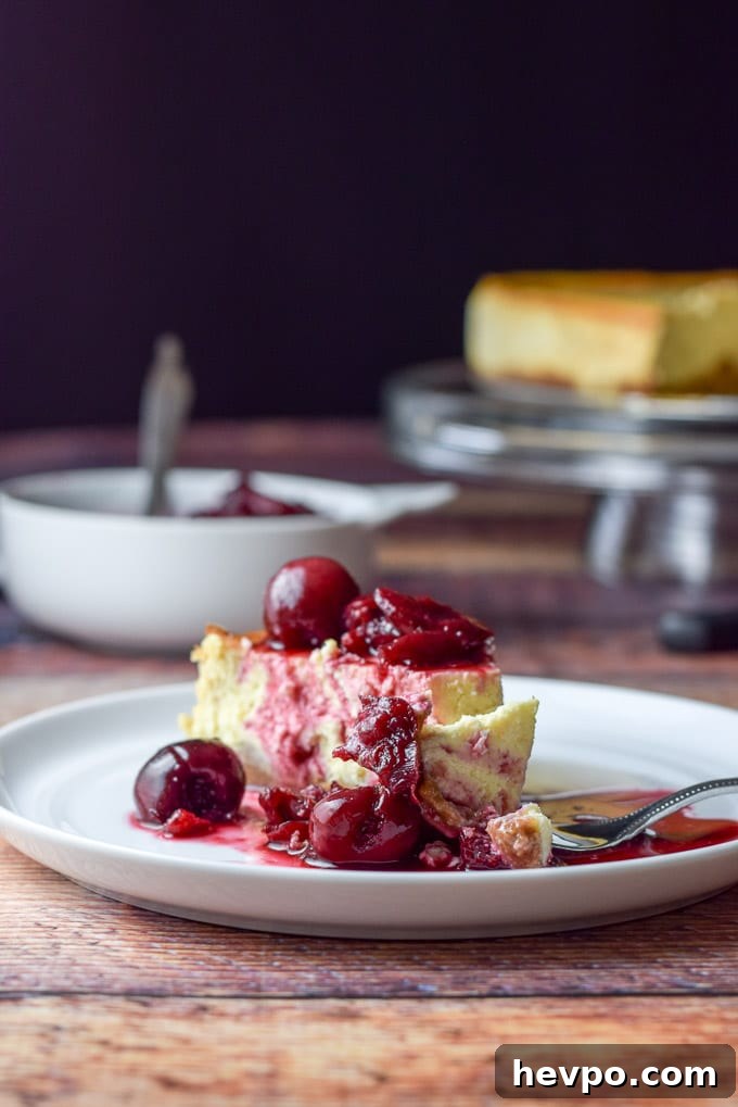 A small plate with the cheesecake covered with cherries and a fork with a bite laying on the plate