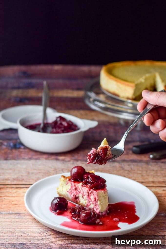 A hand holding a fork with a bite of cheesecake on it. It is held over the plate