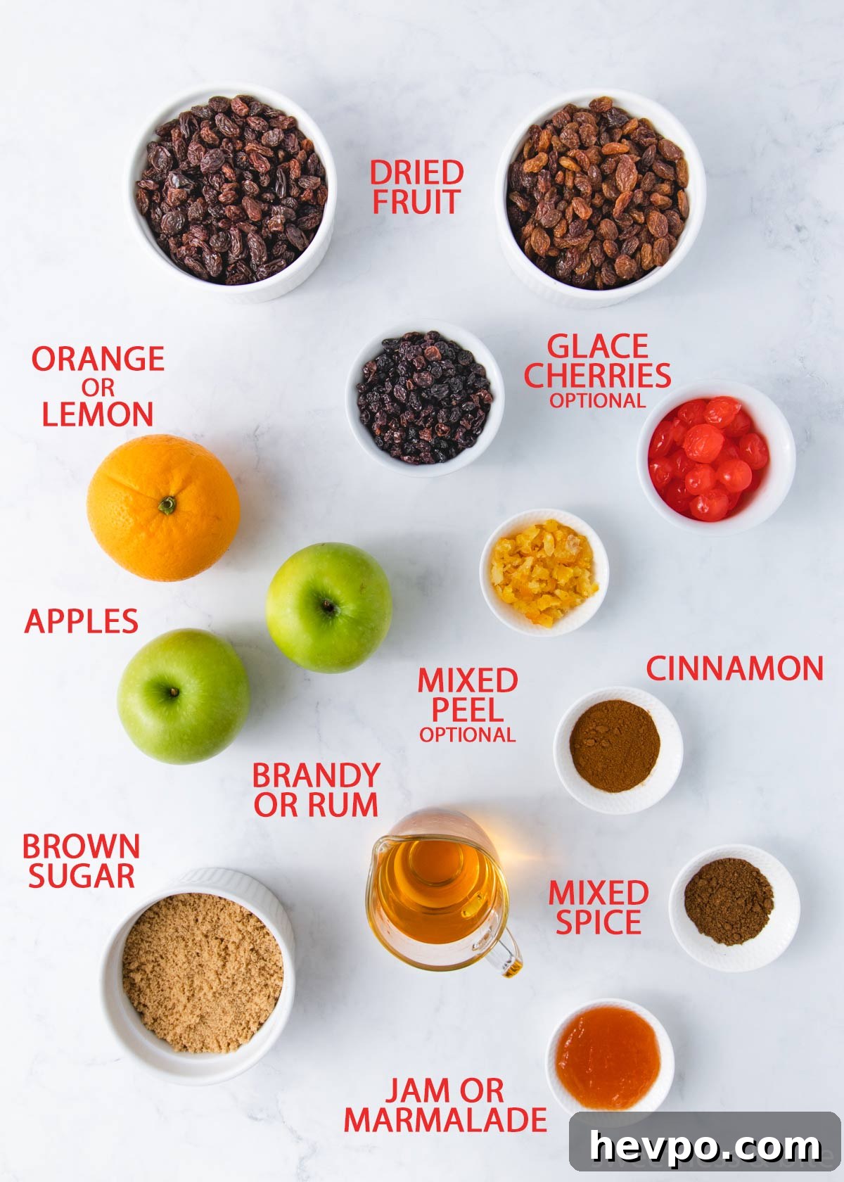The fruit mince ingredients laid out on a grey marble background with labels - dried fruit, cherries, orange, mixed peel, apples, spices, brown sugar, rum and jam.
