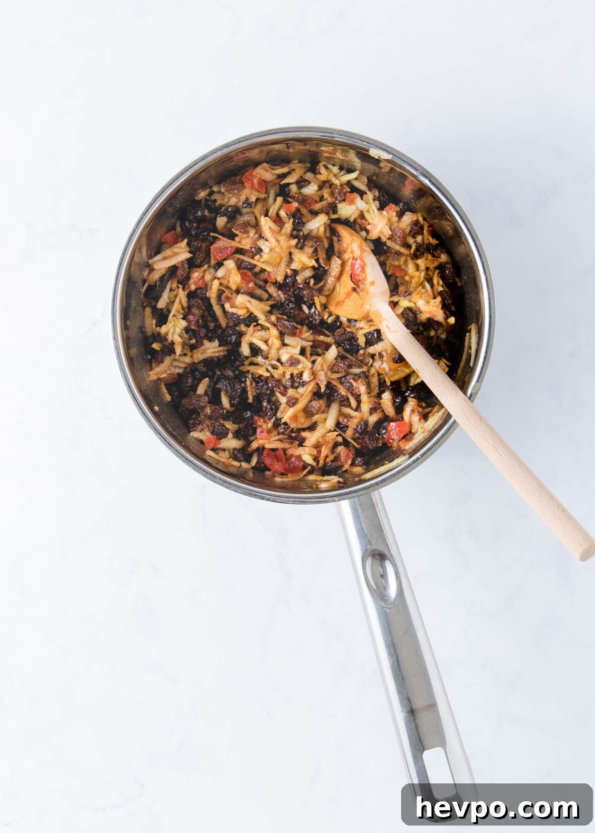 All of the fruit mince ingredients stirred together in a pan with a wooden spoon.