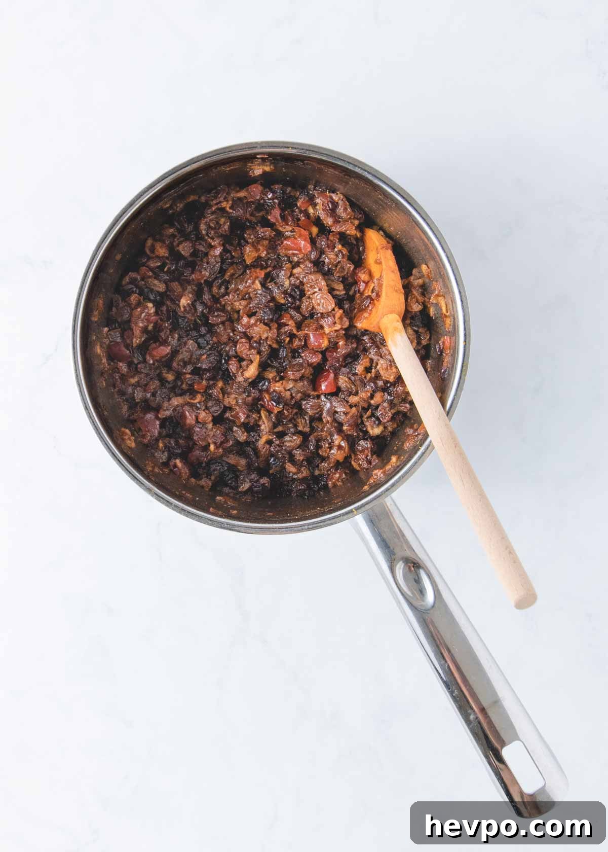 The cooked fruit mince in a pan with a wooden spoon.