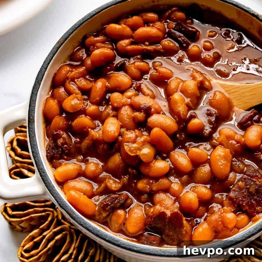 Maple Bacon Recipe with Just 2 Ingredients 16 Up close image of a pot of baked beans with a wooden spoon.