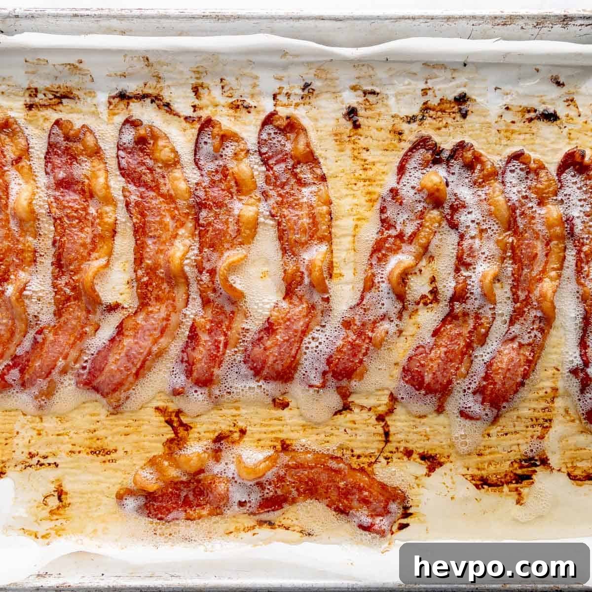 Maple Bacon Recipe with Just 2 Ingredients 5 Strips of crispy bacon on a baking sheet lined with parchment paper.