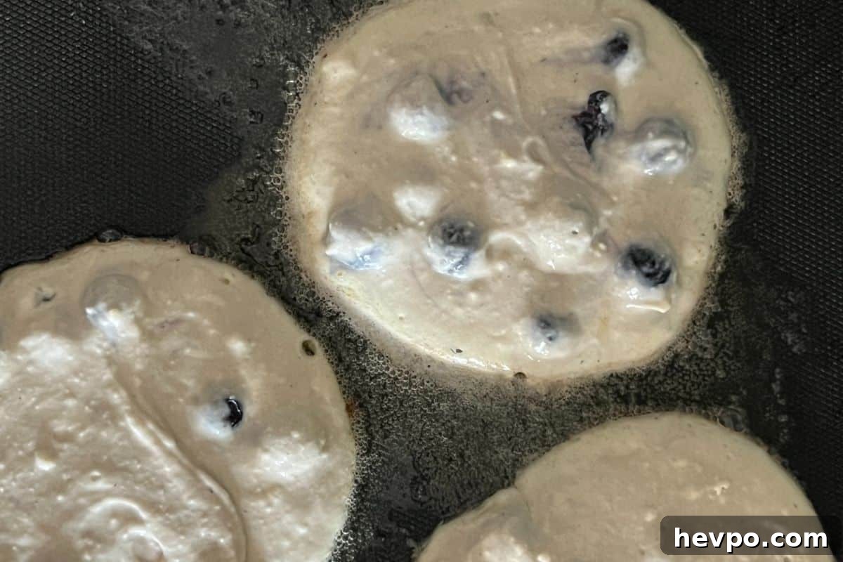 Trisha Yearwood’s Famous Blueberry Pancake Recipe 5 Blueberry pancakes cooking on a griddle.