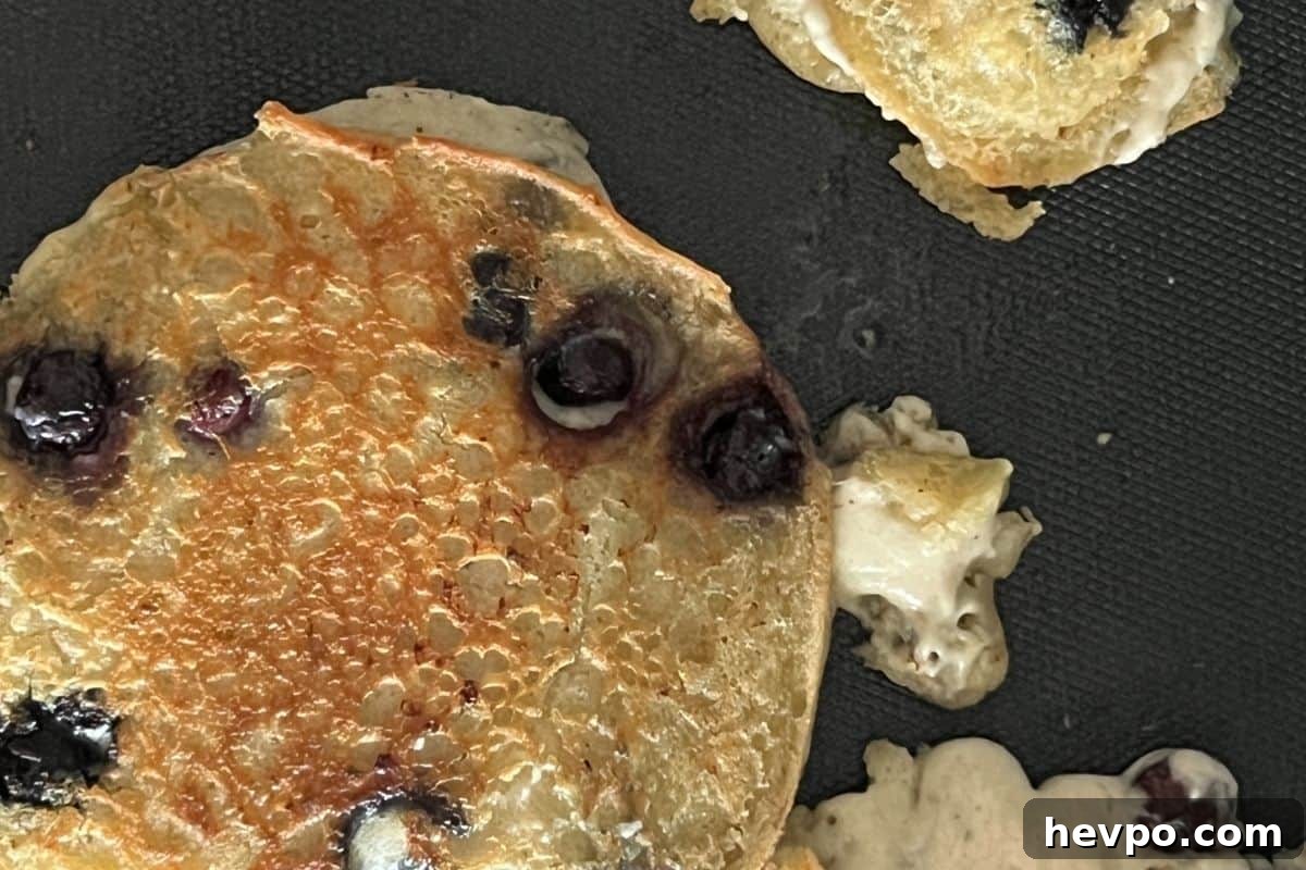 Trisha Yearwood’s Famous Blueberry Pancake Recipe 6 Blueberry pancakes cooking on a griddle.