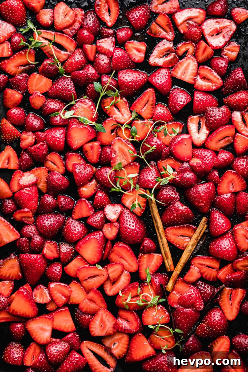 Roasted Strawberries: How to Cook and Use Them for Bold Flavor 7 sliced strawberries with sugar, cinnamon sticks, vanilla and thyme on a baking sheet.