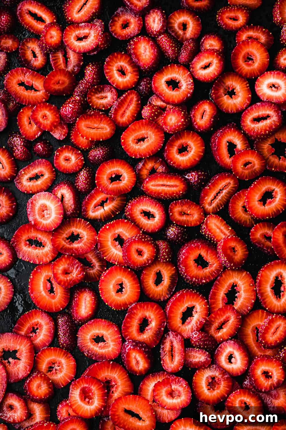 Roasted Strawberries: How to Cook and Use Them for Bold Flavor 9 Overhead shot of sliced strawberries on a dark sheet pan before roasting, arranged in a single layer showing their vibrant red flesh and seeds.