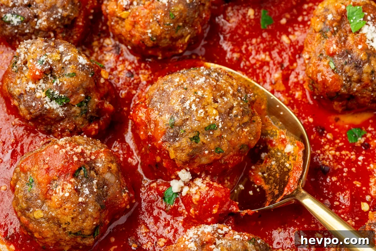 Close up view of spicy meatballs made with ground beef, Italian sausage and gluten-free breadcrumbs resting in a red marinara sauce and being scooped out with a gold spoon.