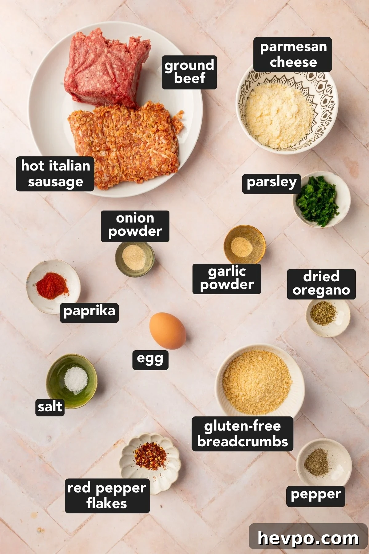 Image of ground beef, Italian sausage, gluten-free breadcrumbs, an egg, parmesan cheese, fresh parsley, dried oregano, garlic powder, onion powder, paprika, salt, ground black pepper, and red pepper flakes, each in their own bowls resting on a brick countertop.