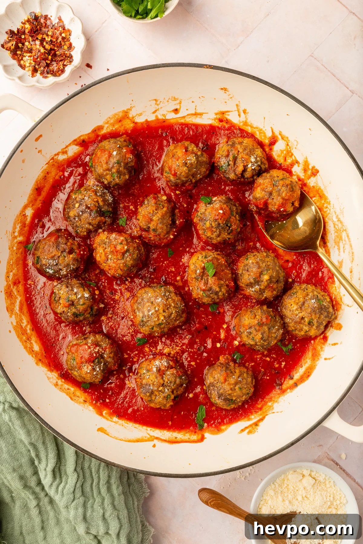 Spicy ground beef, Italian sausage and gluten-free breadcrumb meatballs resting in marinara sauce in a beige bowl on a table with various ingredients.