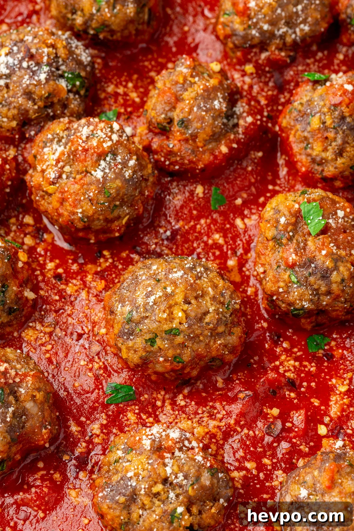 Close up image of spicy ground beef, Italian sausage, and gluten-free breadcrumb meatballs resting in a red marinara sauce.