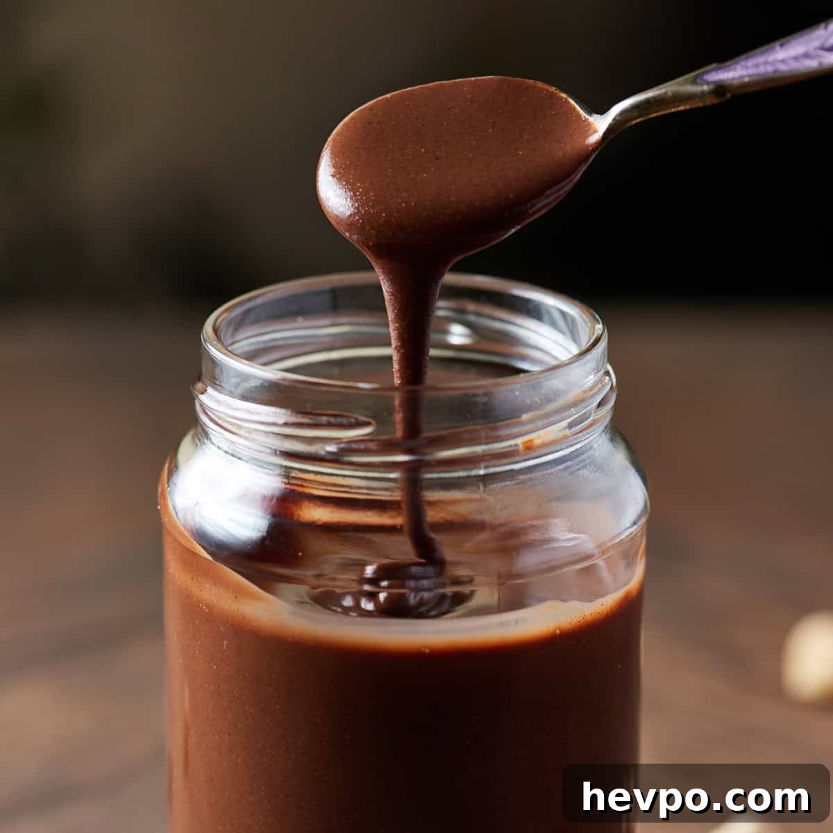 Square photo showing a close up of the spoon of chocolate hazelnut butter dripping into the jar.