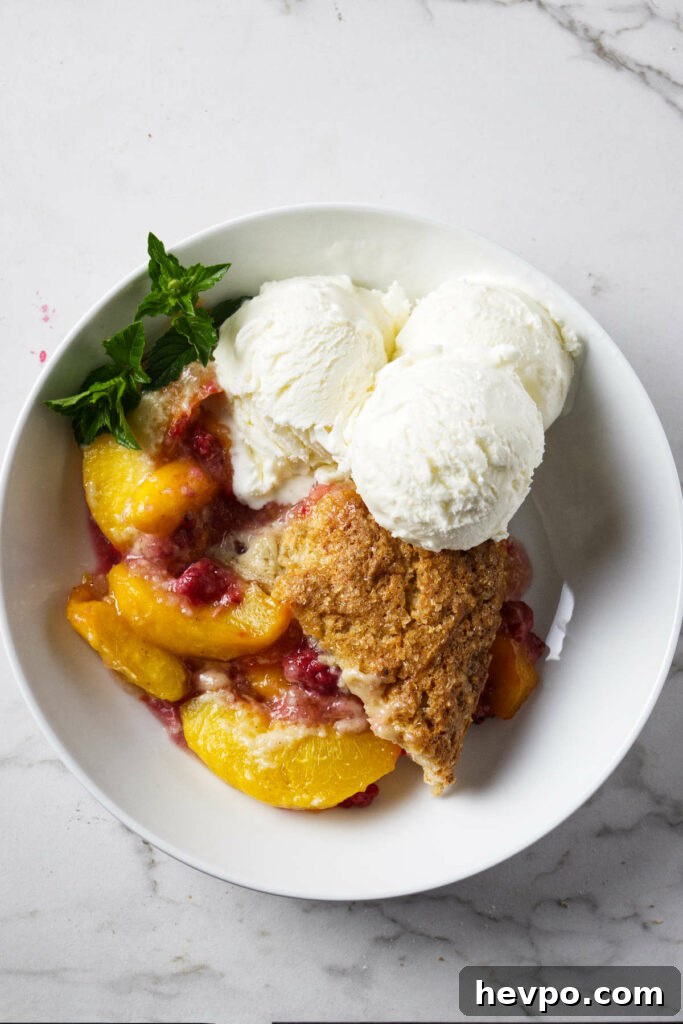 Raspberry and Peach Cobbler with Buttermilk Drop Biscuits 8 A serving of peach raspberry cobbler in a bowl with ice cream.