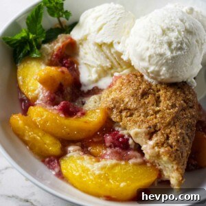 Raspberry and Peach Cobbler with Buttermilk Drop Biscuits 9 Raspberry peach cobbler with buttermilk biscuits in a bowl with ice cream.