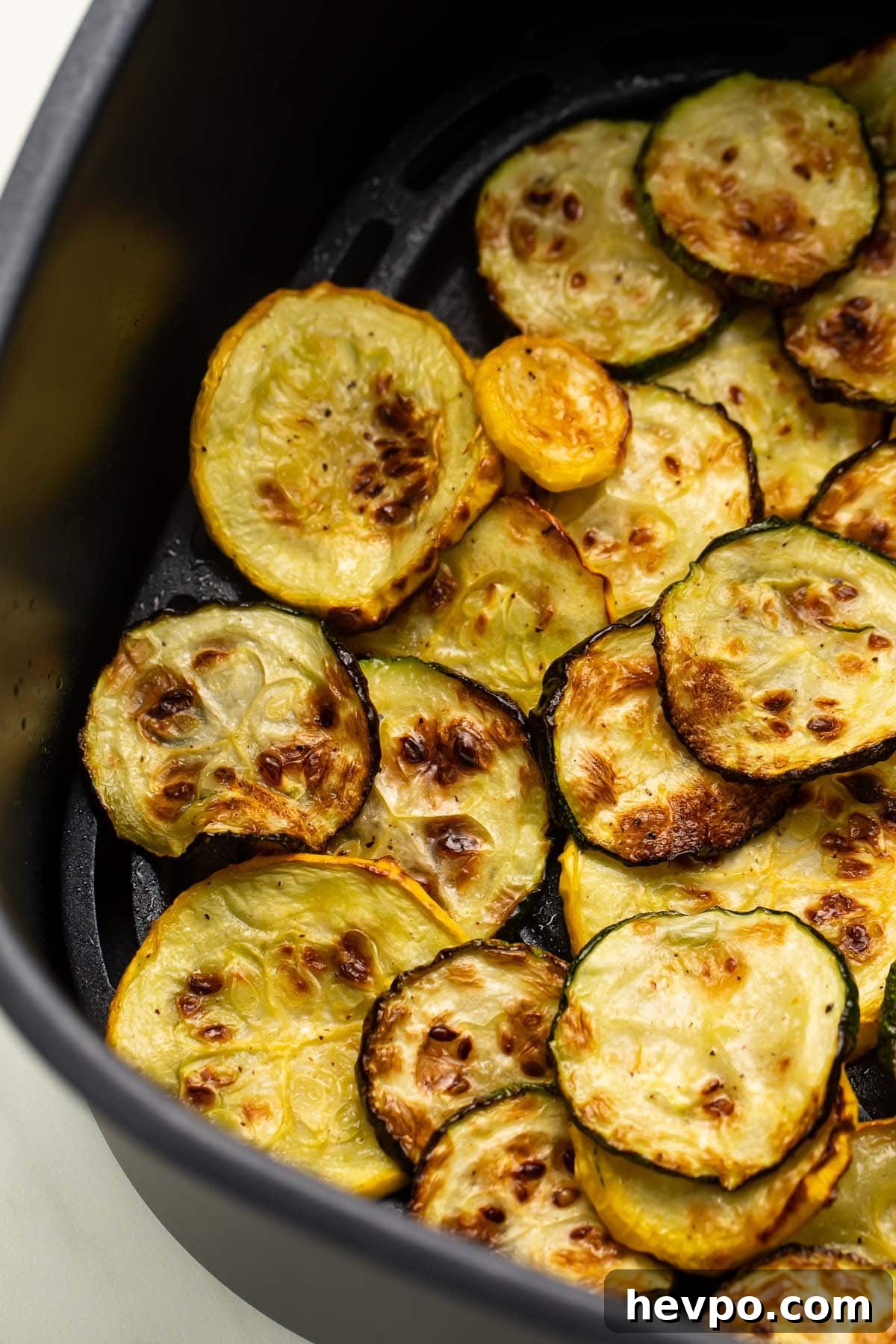 Crispy Air Fryer Squash Recipe — Quick Roasted Slices 3 Several discs of yellow and green squash in an air fryer basket.