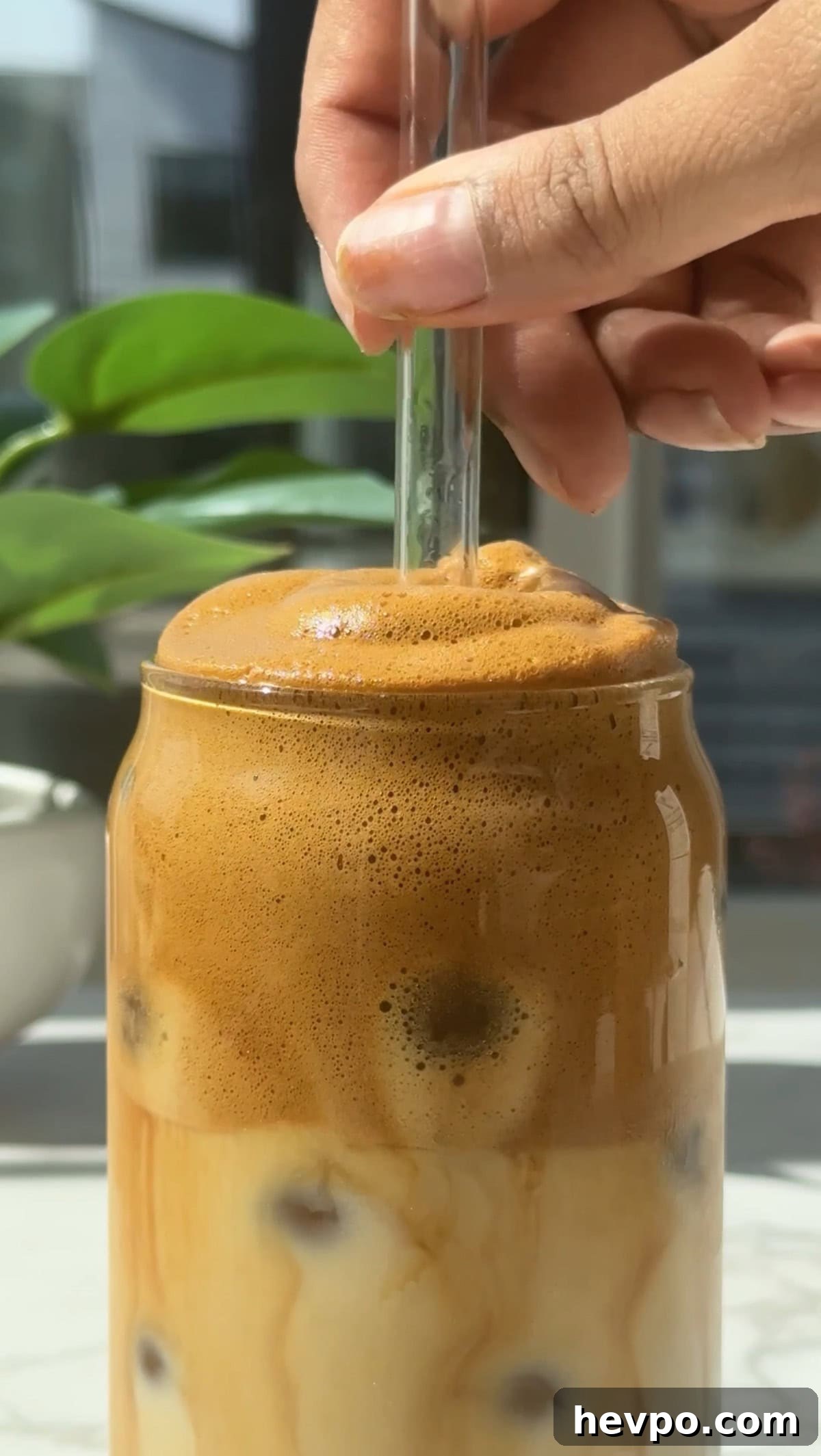 Whipped honey coffee in a glass with a clear straw inside it.