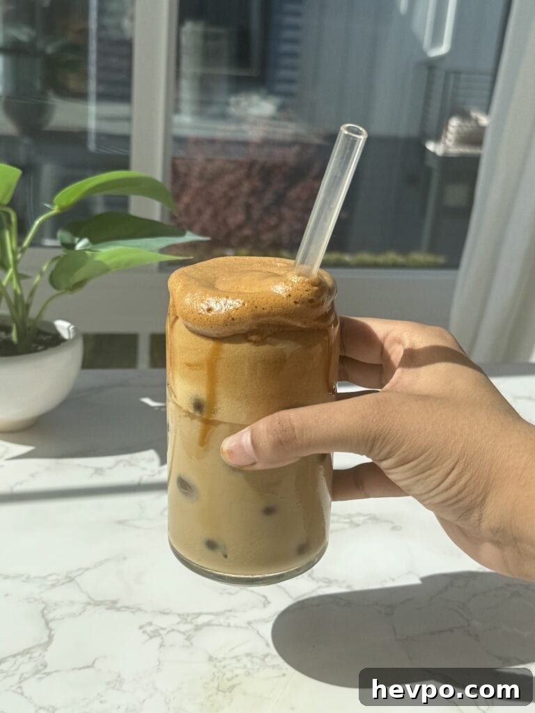 A hand holding a clear glass filled with whipped honey coffee.
