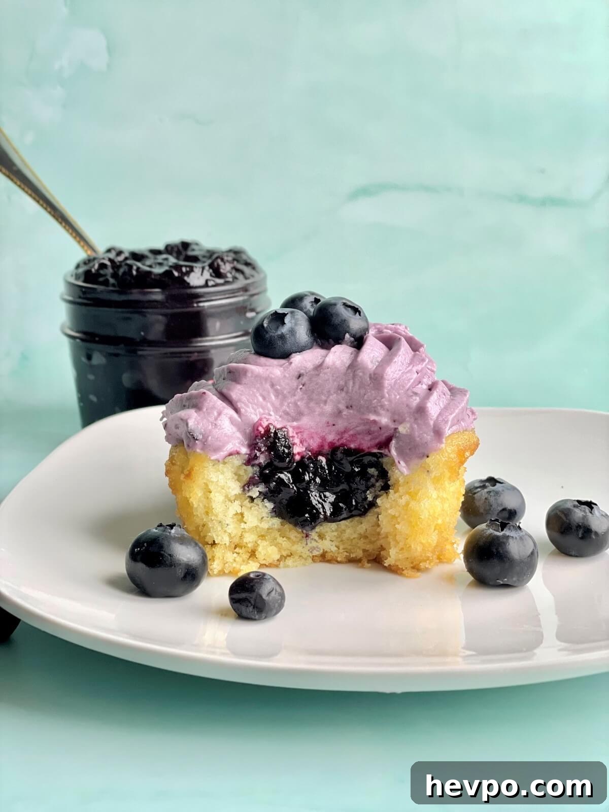 a vanilla cupcake with blueberry cupcake filling and a bowl of blueberry compote filling in the background